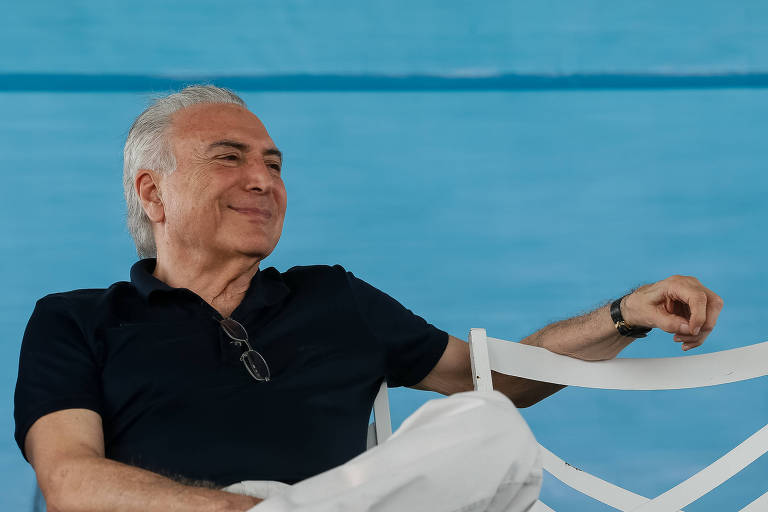 Presidente Michel Temer, de camisa polo preta e calça branca, sentado de pernas cruzadas e braço esquerdo apoiado numa cadeira branca  