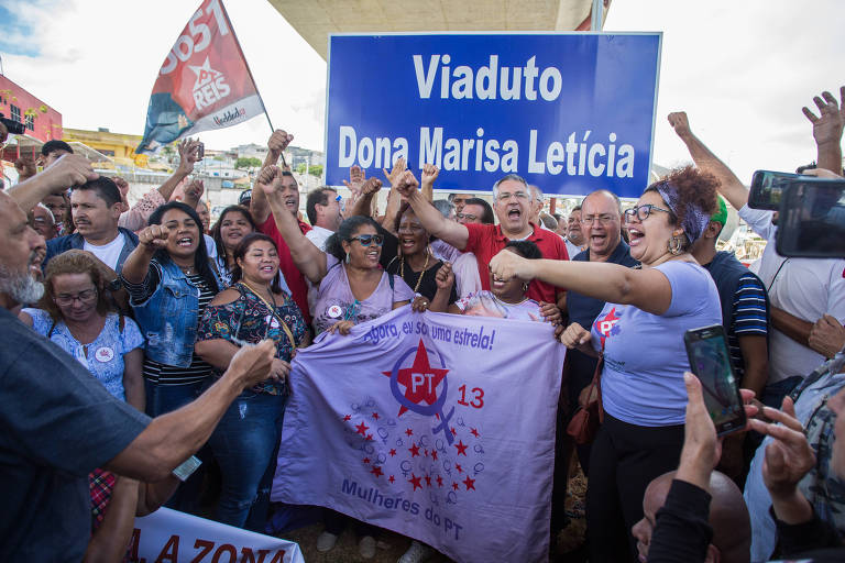 Militantes do PT vestidos de lilás e vermelho e de braços levantados diante da placa azul "viaduto Dona Marisa Letícia"